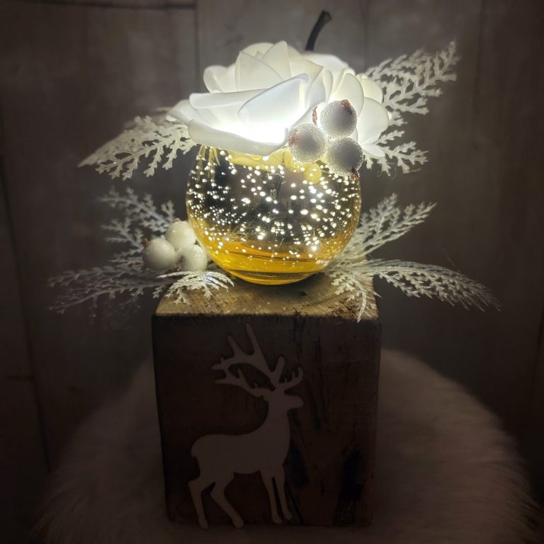 Vase décoratif lumineux avec fleurs blanches et feuillage sur un support en bois.