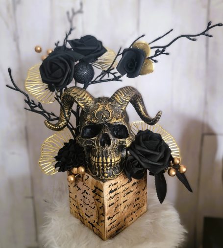 Buste décoratif avec crâne, fleurs noires et dorées, et éléments naturels.