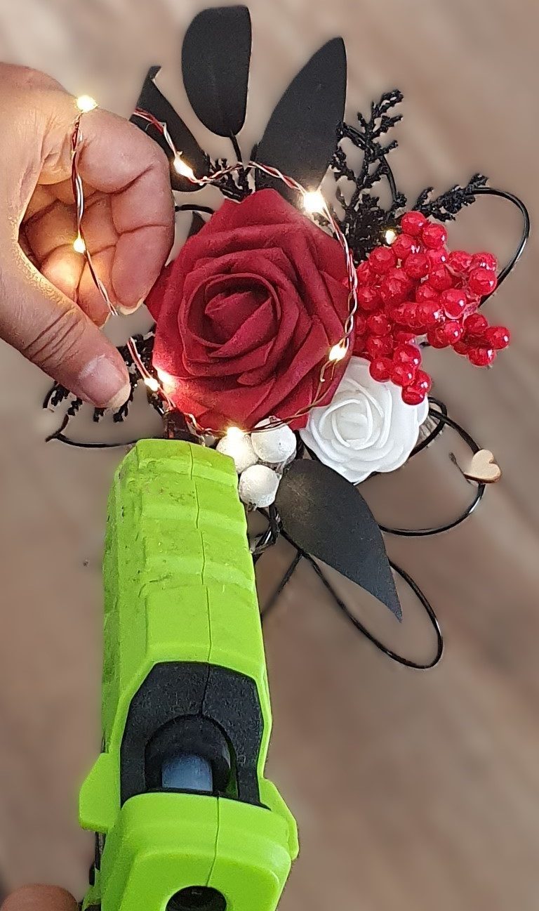 Main dans un gant tenant une fleur rouge et des lumières en décor, avec un pistolet à colle.