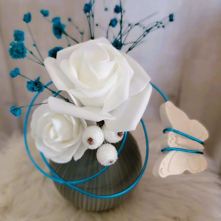 Vase avec des roses blanches, fleurs bleues et un papillon décoratif.