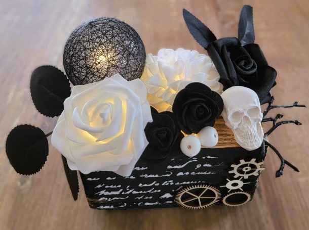 Composition de fleurs noires et blanches, avec une touche de lumière et une décoration en crâne.