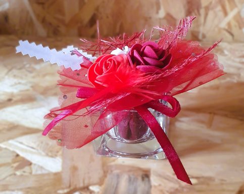 Petit cadeau décoré de fleurs en papier rose et rouge dans un emballage transparent.