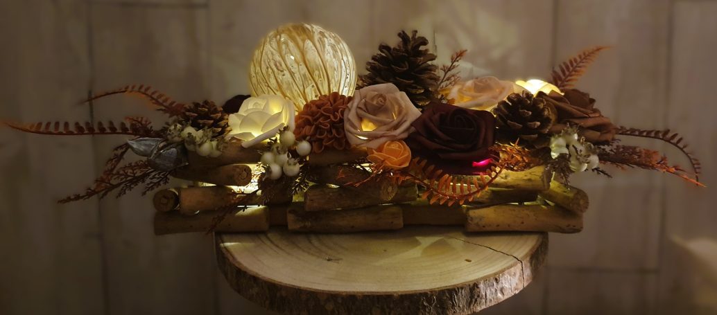 Arrangement de fleurs séchées et cônes de pin, éclairé par des lumières douces.