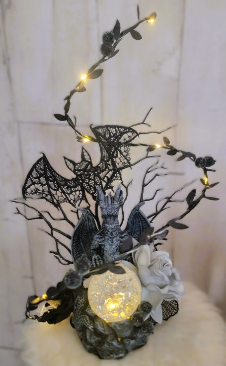 Sculpture sombre avec une créature, des branches noires et des lumières, ornée de toile d'araignée.