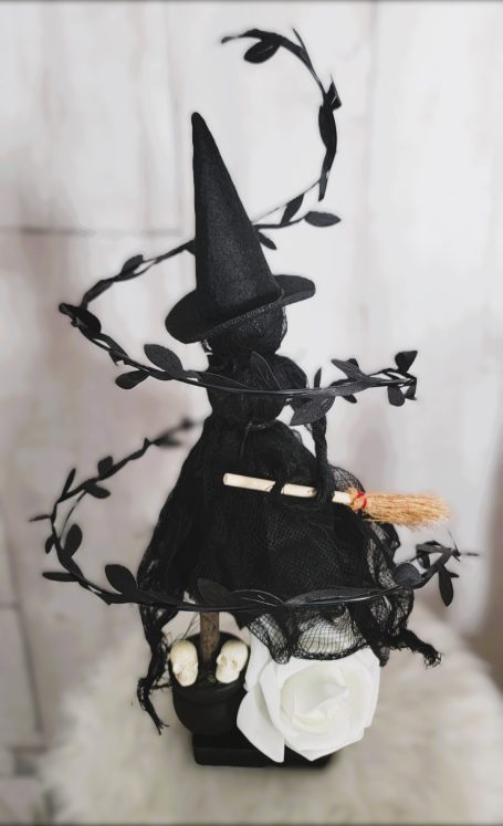 Sorcière en noir avec chapeau, spiralée de branches, tenant un balai.