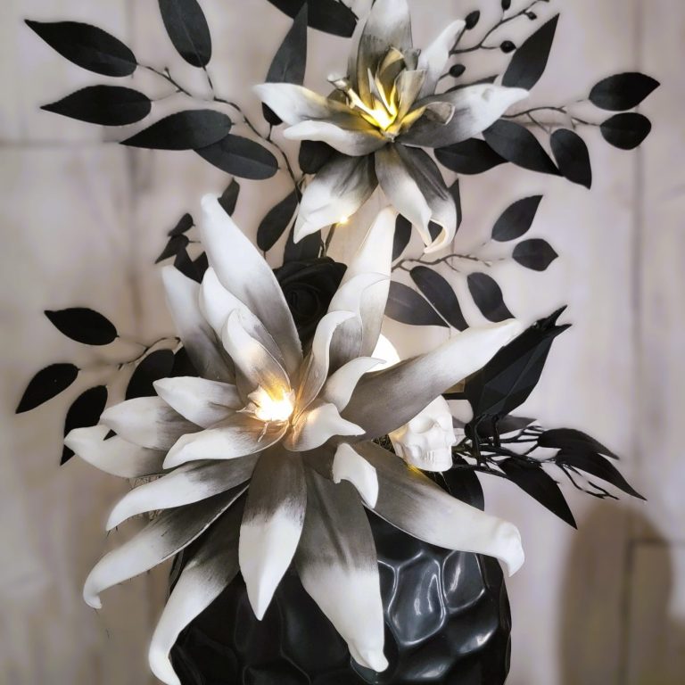 Fleurs en papier noir et blanc avec feuillage, illuminées par des lumières douces.
