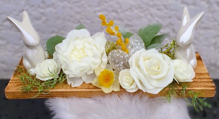 Composition de fleurs blanches avec des lapins en céramique sur une planche en bois.