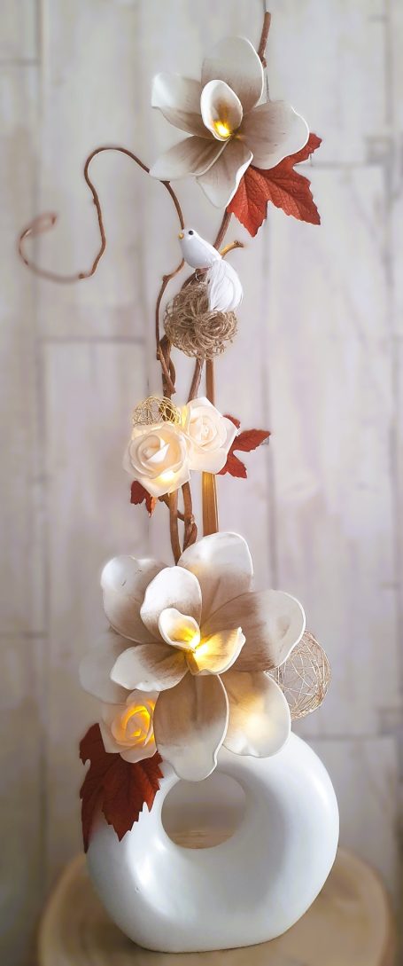 Vase blanc avec des fleurs blanches et beige, branches et feuilles colorées.