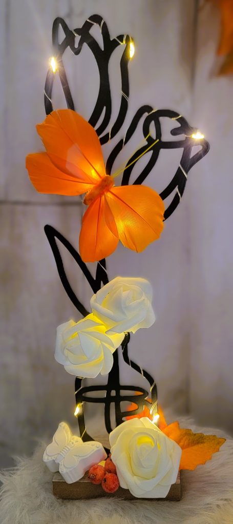 Vase à fleurs avec roses blanches, ruban orange et lumières suspendues.