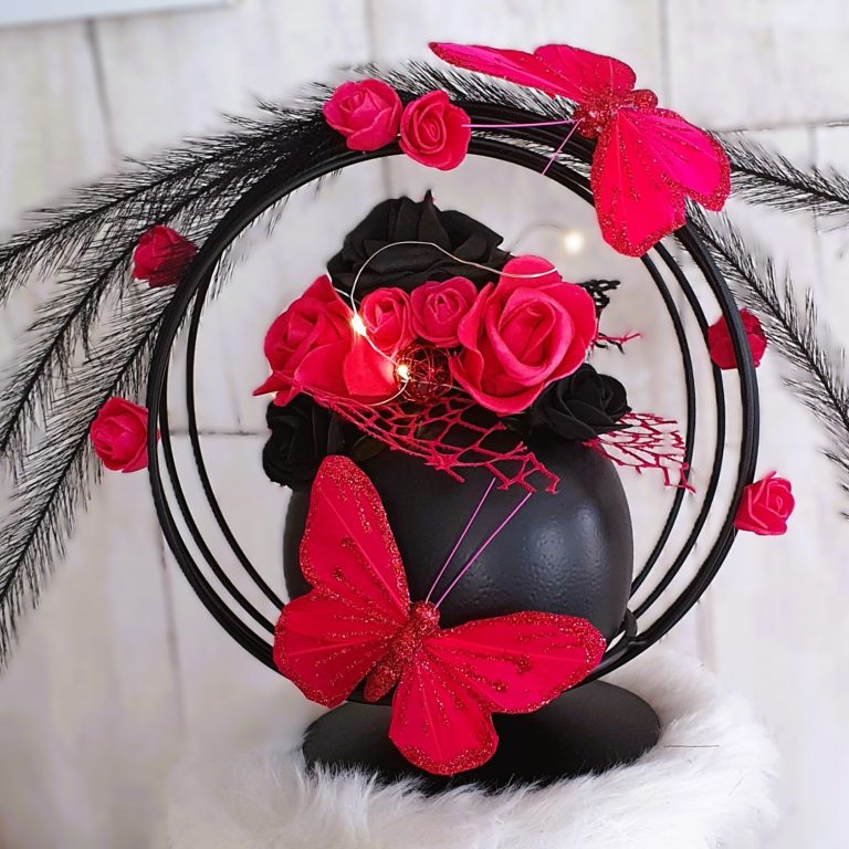 Arrangement de roses noires et rouges avec des papillons et des plumes, sur un support noir.