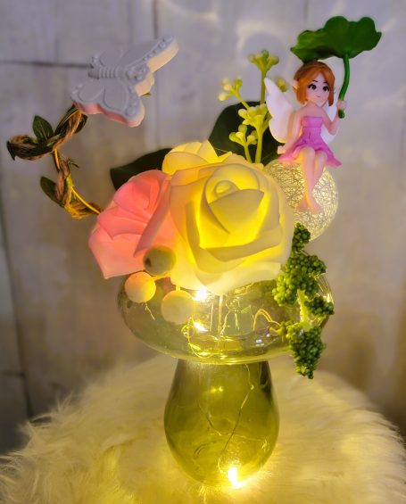 Fleurs colorées et une fée, le tout dans un vase avec des lumières.