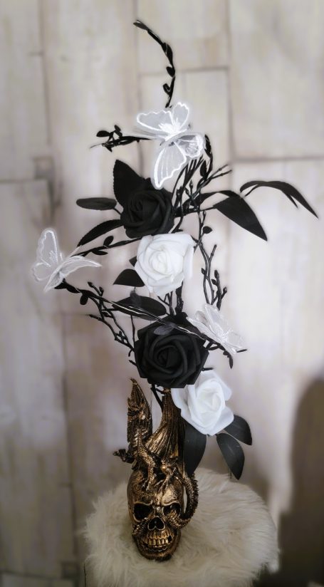 Arrangement de fleurs blanches, noires et argentées dans un vase doré.