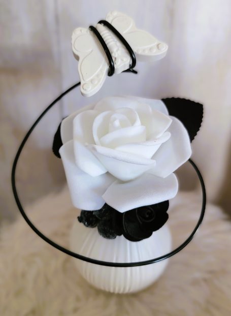 Fleur en plastique blanche avec un papillon noir, décorée de fleurs noires.
