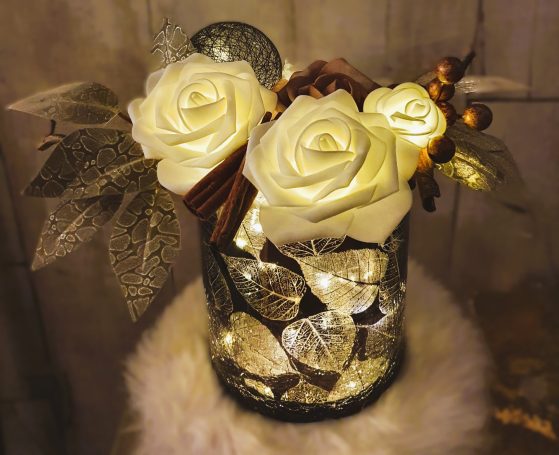 Vase décoratif avec des roses blanches, des feuilles et des pierres brillantes.