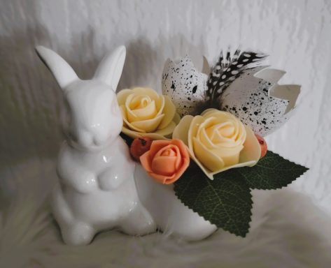 Un lapin en céramique blanc à côté d'un bouquet de roses de différentes couleurs.